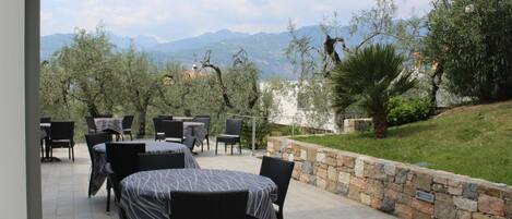 Un patio al aire libre con mesas y sillas, un muro de piedra y vistas a las montañas.