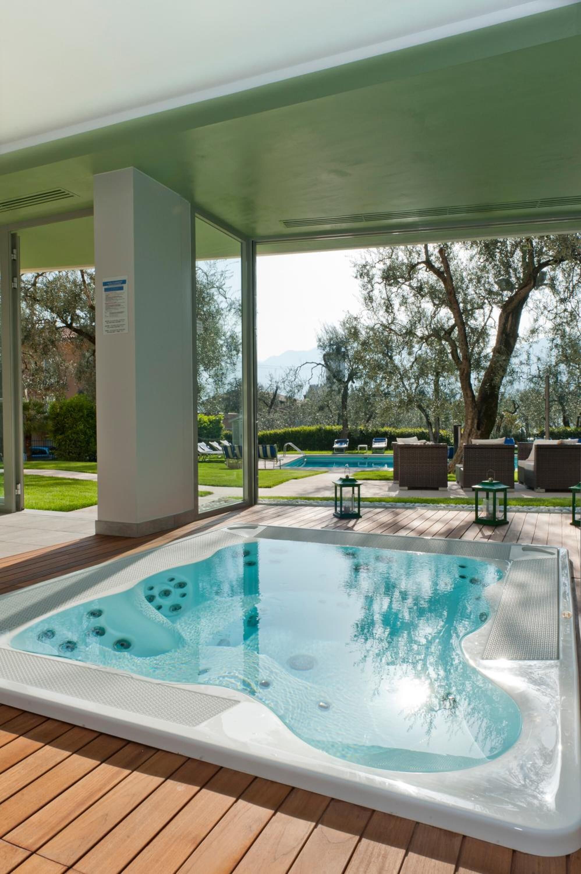 A hot tub with a view of a swimming pool and trees in the background.