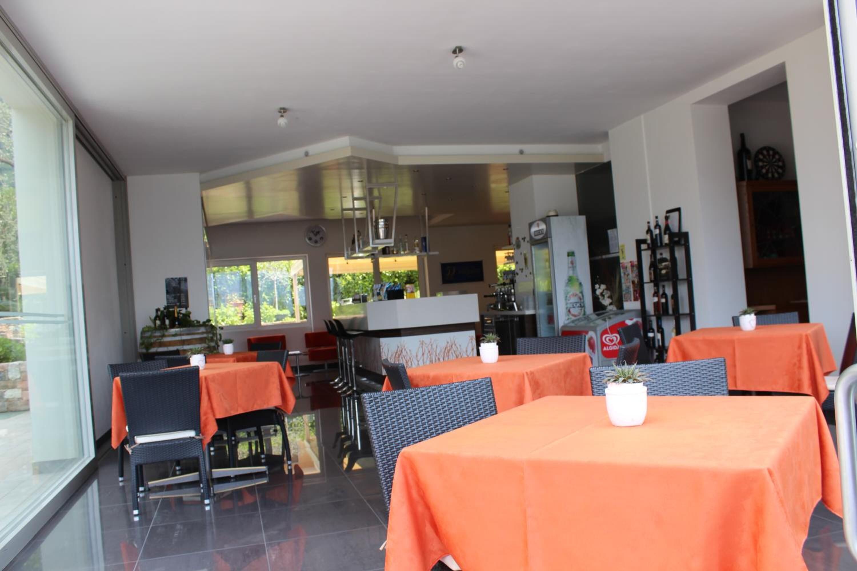 A restaurant with tables covered in orange tablecloths, black chairs, and a glass partition.