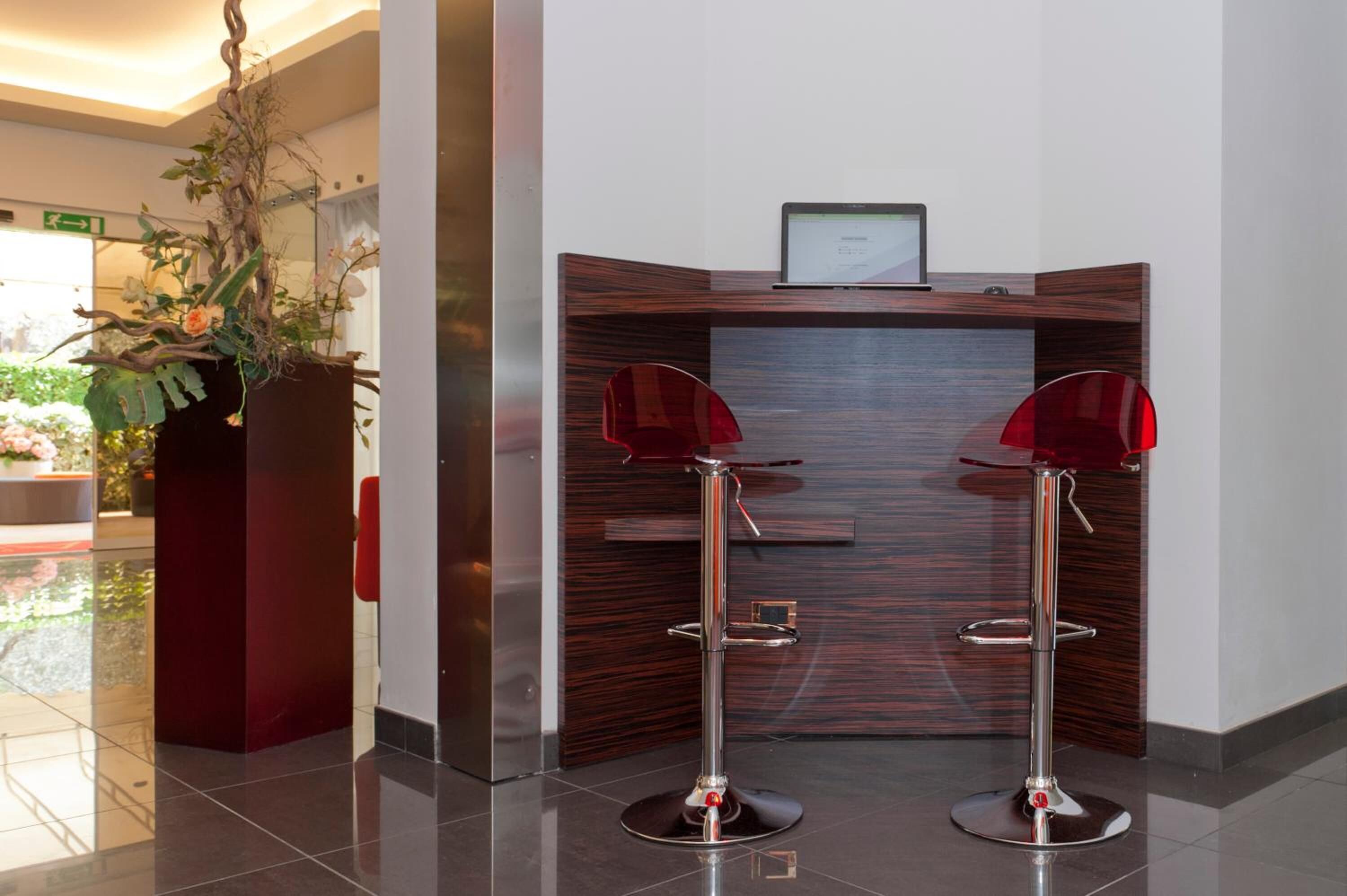 Un'area di accoglienza con una reception in legno, due sgabelli rossi e una pianta in vaso con fiori.