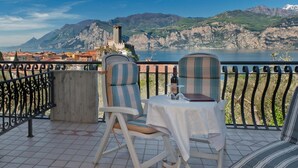 A terrace with two chairs and a table, overlooking a mountainous landscape and a body of water. - Hotel Augusta (Malcesine)