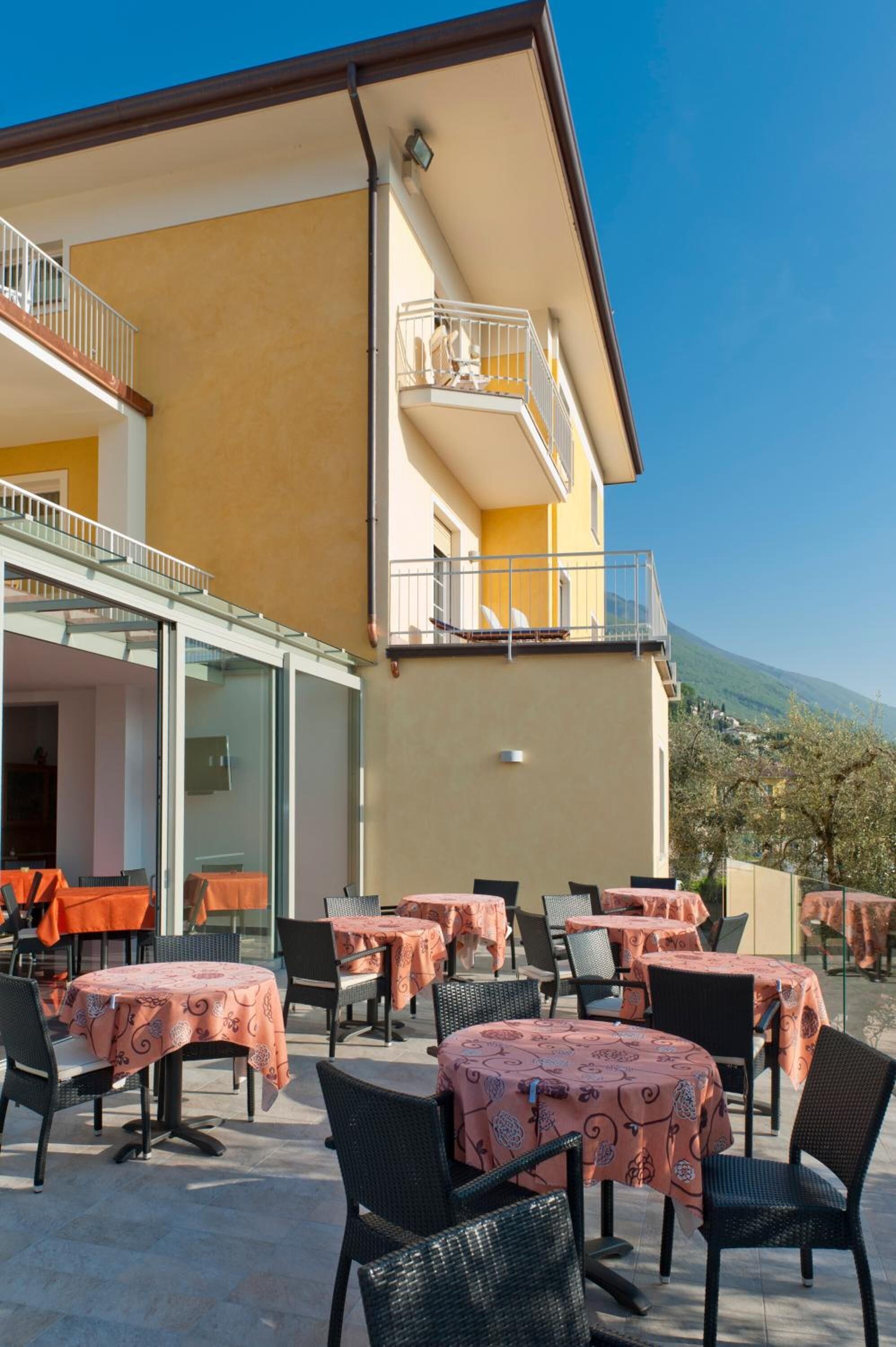 An outdoor patio with tables and chairs, a glass door entrance, and a balcony with railings.
