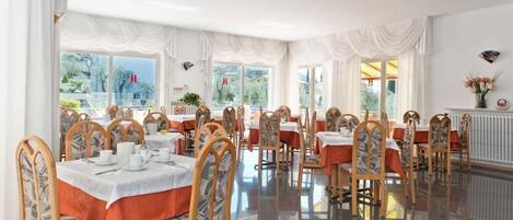 A dining area with tables set for service, chairs with patterned upholstery, and large windows offering a view of the outside.