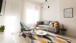 Ein modernes Wohnzimmer mit einer Couch, einem Glastisch, einem Sessel und einer Topfpflanze.