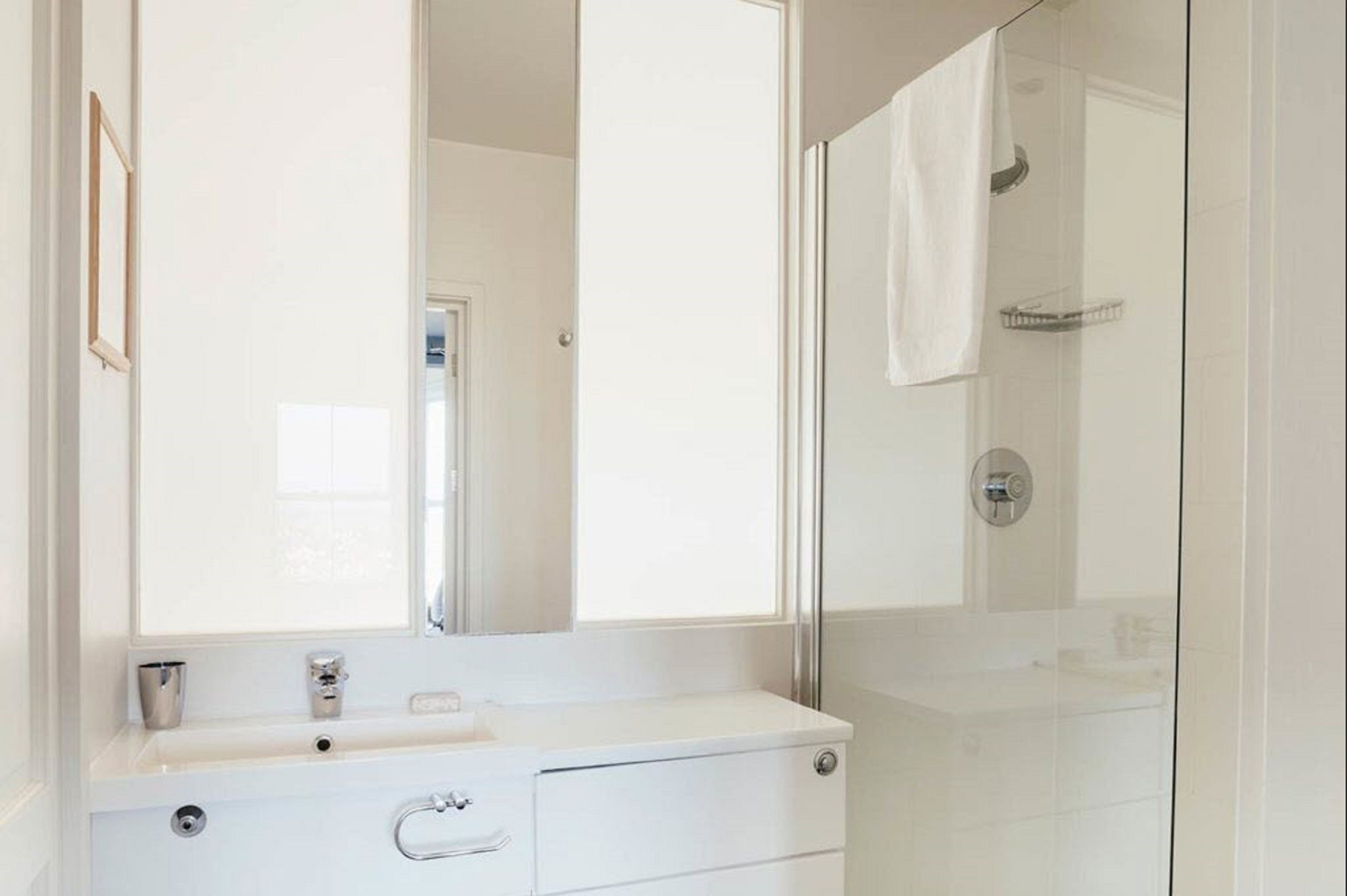 A modern bathroom with a large mirror, a sink, and a glass shower enclosure.