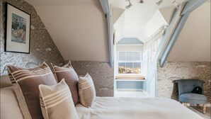 Una camera da letto con un letto, cuscini, una sedia e una finestra vista.