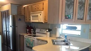 A kitchen with wooden cabinets, a stainless steel refrigerator, a microwave, a stove, and a sink. - Enjoy "Island Cabana" (Jensen Beach)