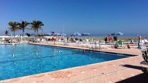 A swimming pool with lounge chairs and umbrellas, palm trees, and a clear sky. - Enjoy "Island Cabana" (Jensen Beach)