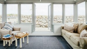 Et orangeri med udsigt til en stenvæg, to sofaer, et sofabord og et lille bord med bøger og kopper.