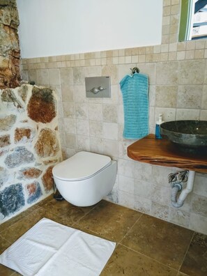 Een badkamer met een stenen muur, een wit toilet, een houten wastafel en een handdoek aan de muur.