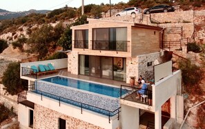 Een modern huis met twee verdiepingen, een zwembad, stenen muren en een balkon met blauwe kussens.