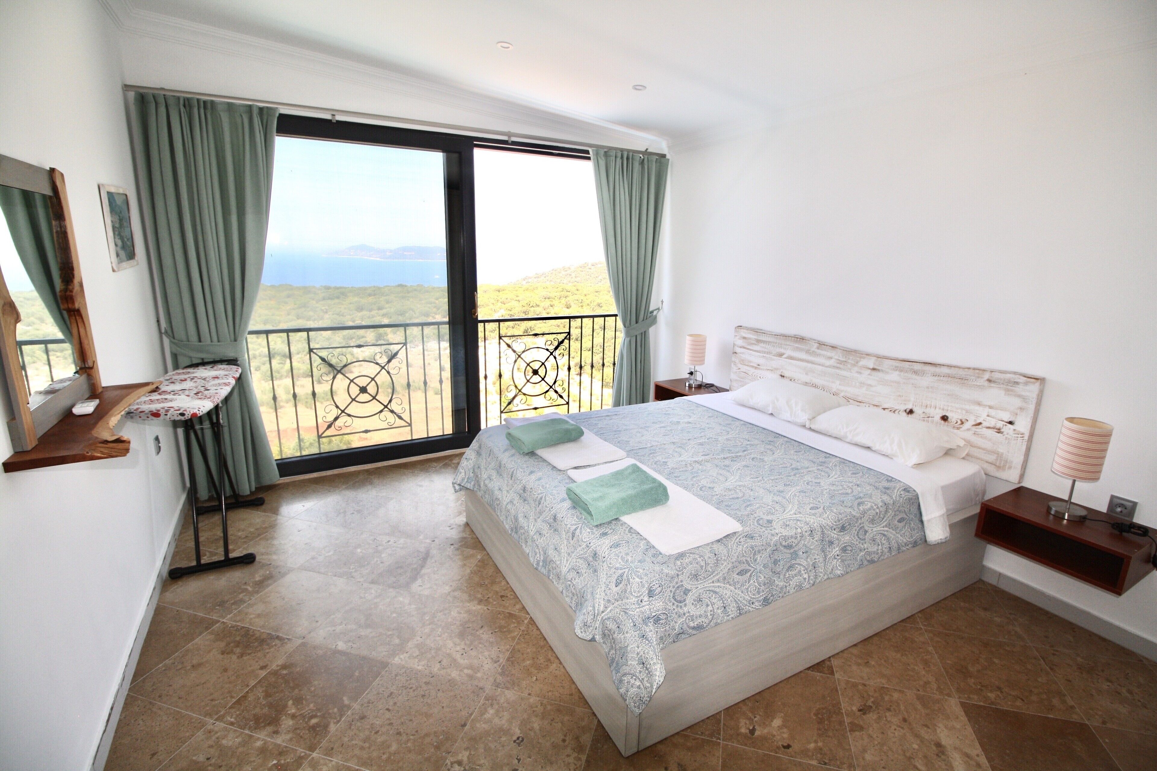 A bedroom with a large bed, a balcony, and a view of the landscape.