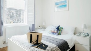 A neatly arranged bedroom with a bed, bedside tables, a window, and a painting on the wall. - 10 Fernlea Court (St Ives)