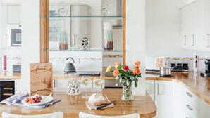 A modern kitchen with a wooden countertop, a glass shelf unit, and a vase with flowers. - 10 Fernlea Court (St Ives)