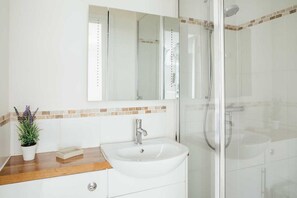 A bathroom with a white sink, a mirror, and a shower area. - 10 Fernlea Court (St Ives)