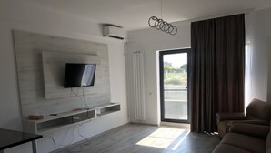 A modern living room with a flat-screen TV mounted on a wall, a sofa, a coffee table, and a sliding glass door leading to an outdoor area. - Beautiful SeaSide Apartments (Mamaia-Sat)
