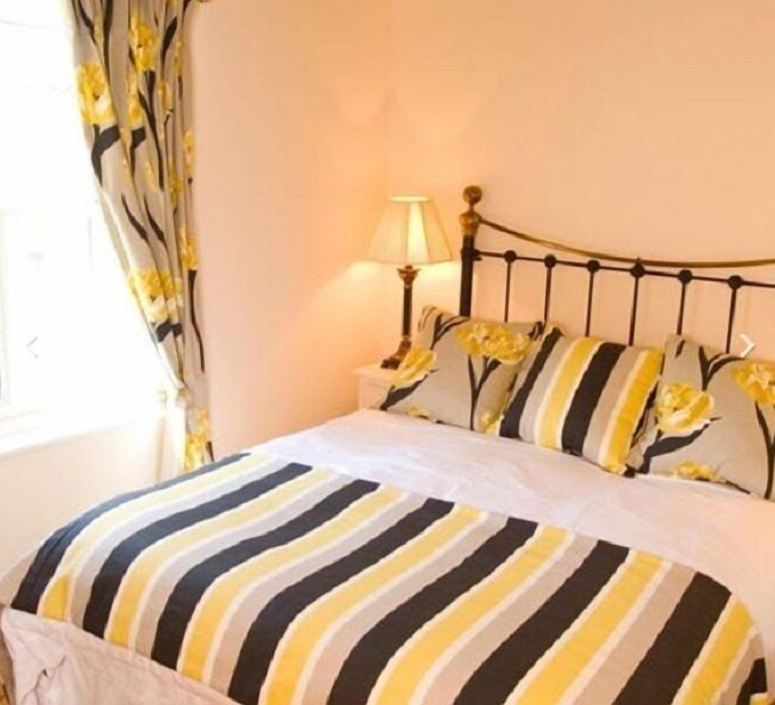 Ein Bett mit gestreifter Bettdecke, ein Nachttisch mit Lampe und blumige Vorhänge.