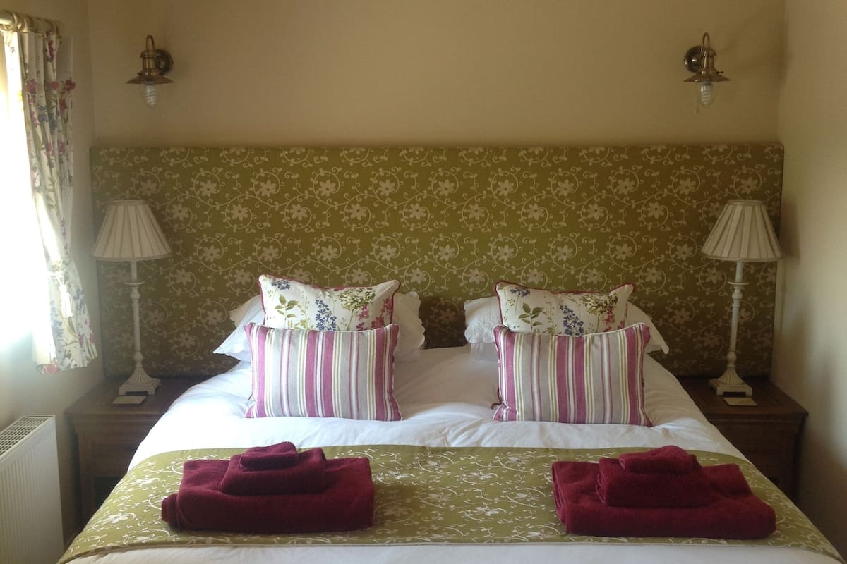 A double bed with floral-patterned headboard, two bedside tables with lamps, and a window with curtains.