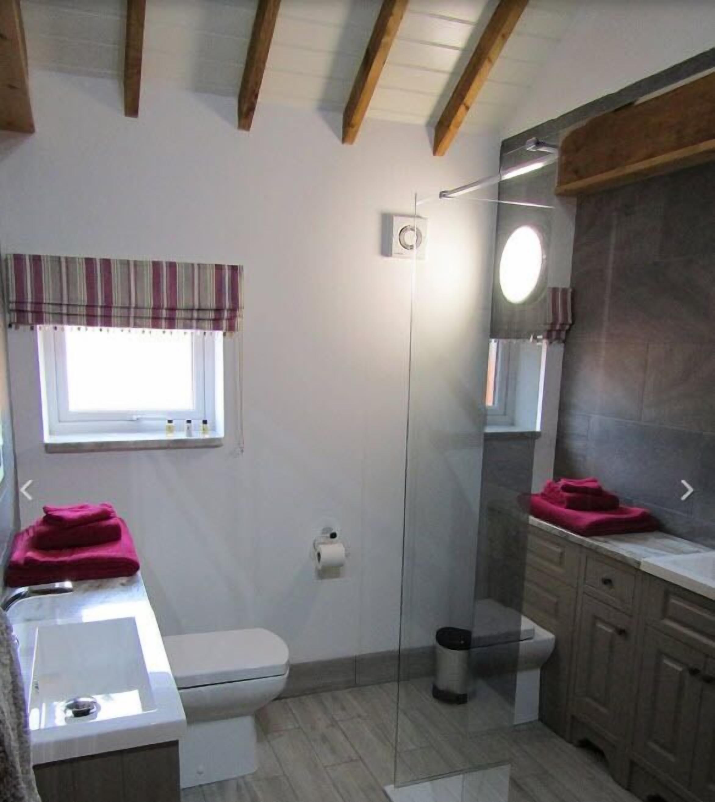 A bathroom with a toilet, sink, and shower. There is a window with curtains, a mirror, and a towel rack.