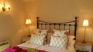 A bedroom with a large bed, two bedside tables, a chandelier, and a brick wall. - Jockhedge Holiday Cottages (Skegness)