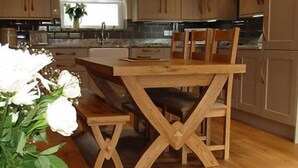A modern kitchen with wooden cabinetry, a central island, and a dining area with a wooden table and chairs. - Jockhedge Holiday Cottages (Skegness)