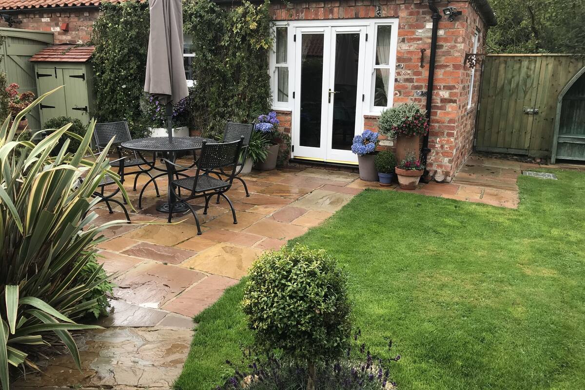 A brick house with a patio area featuring a table and chairs, a small lawn, and potted plants.