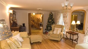 A cozy living room with a wooden floor, a beige sofa, a small armchair, and a Christmas tree. - Jockhedge Holiday Cottages (Skegness)