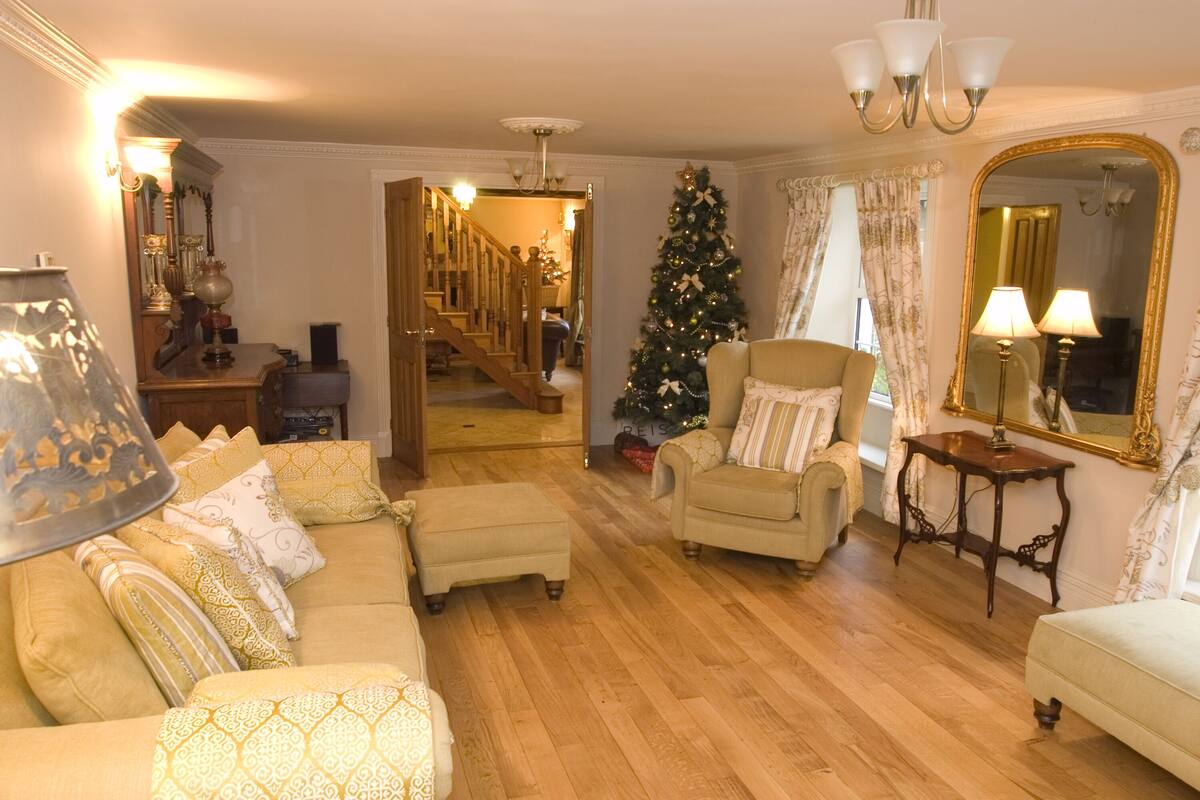 A cozy living room with a wooden floor, a beige sofa, a small armchair, and a Christmas tree.