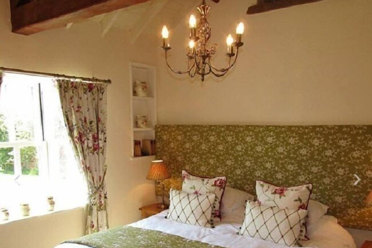 A bedroom with a large bed, floral headboard, and a chandelier.