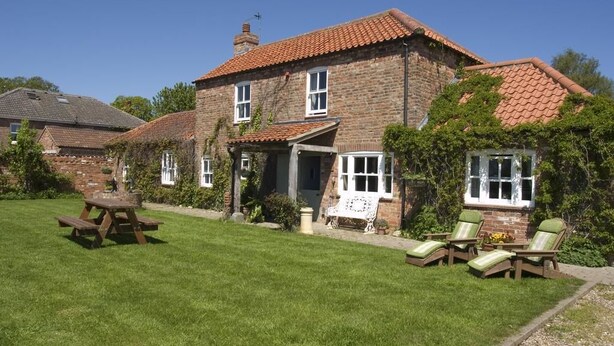 A stone house with a tiled roof, a grassy lawn, and a picnic table. - Jockhedge Holiday Cottages (Skegness)