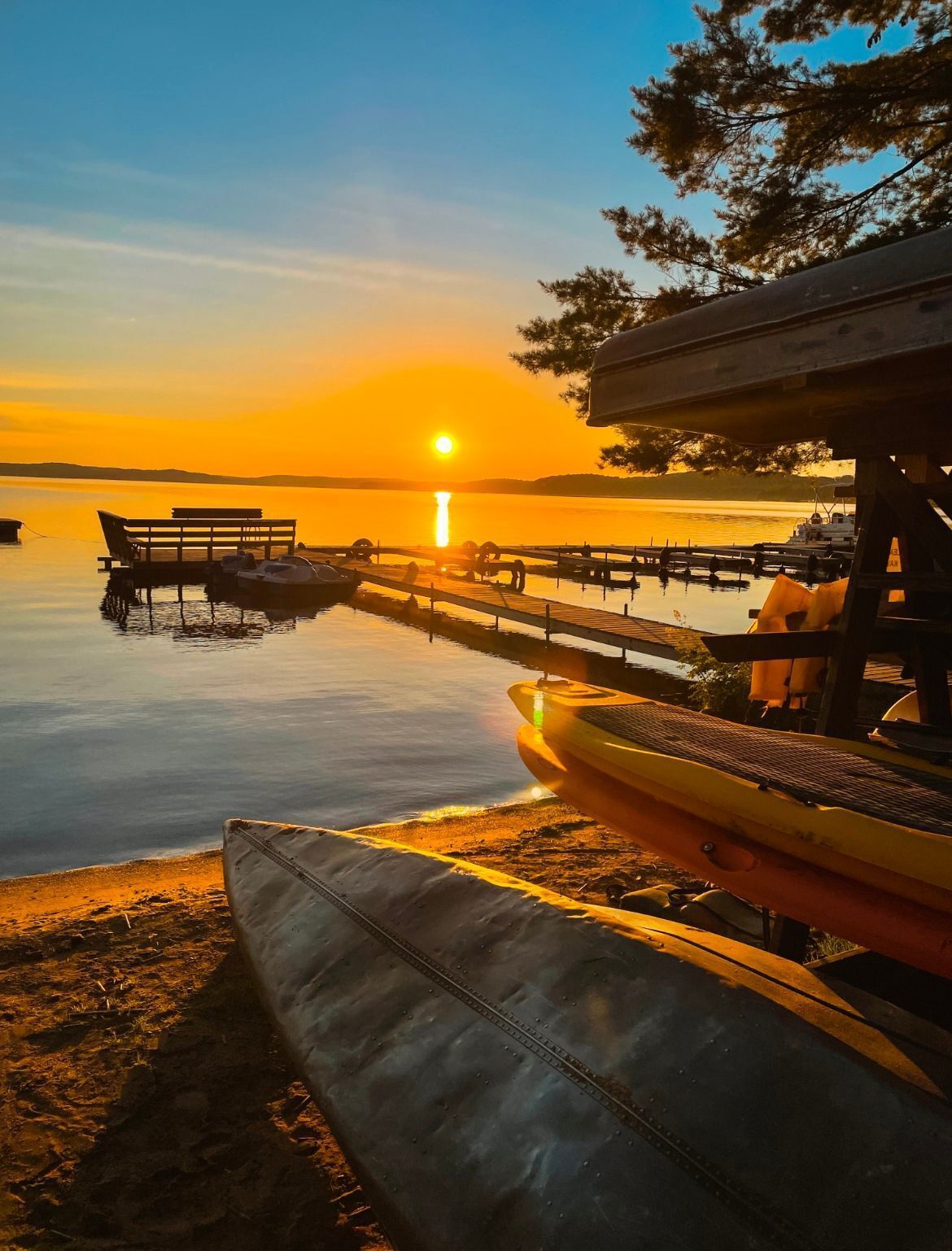 A sunset view over a calm lake with docked boats and a bench.