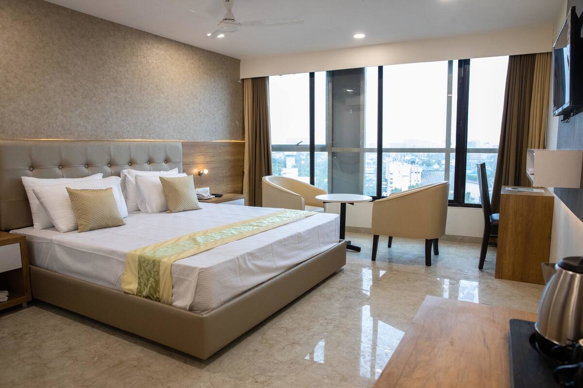 A modern hotel room with a large bed, a desk, and a view of the city.
