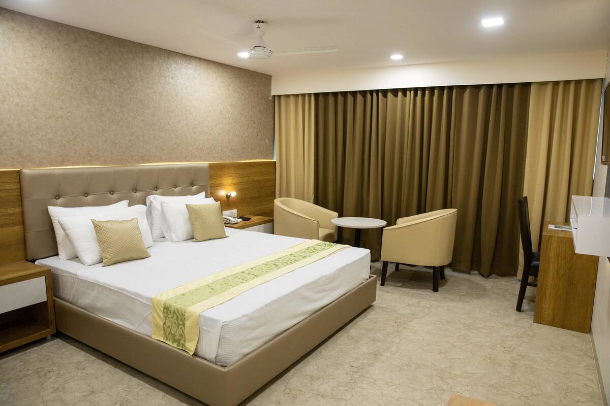 A hotel room with a large bed, a desk, a chair, and a small table.