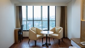 A hotel room with a large window, two armchairs, a small round table, a wooden desk, and a telephone. - Hotel Grace Galaxy (Mumbai)