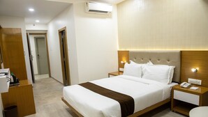 A hotel room with a large bed, wooden headboard, bedside tables with lamps, and an air conditioning unit on the wall. - Hotel Grace Galaxy (Mumbai)