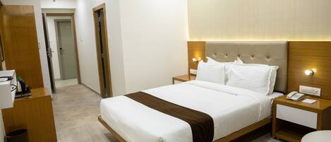 Quarto de hotel com uma cama grande, cabeceira de madeira, mesas de cabeceira com luminárias e um aparelho de ar condicionado na parede.