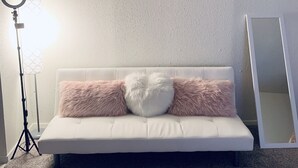 Ein weißes Sofa mit flauschigen Kissen, einem Ringlicht und einem Buddha-Gemälde an der Wand.