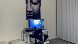 Ein Zimmer mit einem weißen Schreibtisch, einem Computer, einem Stuhl und einem großen Buddha-Gemälde an der Wand.