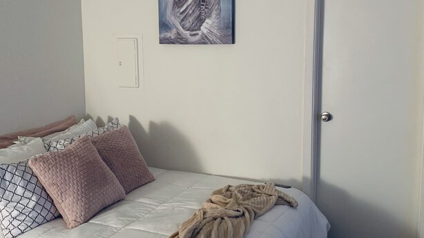 Ein Schlafzimmer mit Bett, Kissen, Decke, einer Tür und einem Wandbild.