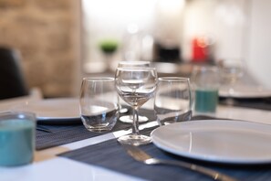 Une table à manger dressée avec des verres transparents, une assiette blanche et une bougie bleue.