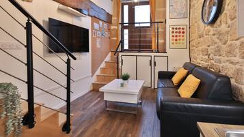 A modern living room with a black leather sofa, a white coffee table, and a staircase with a wooden railing.