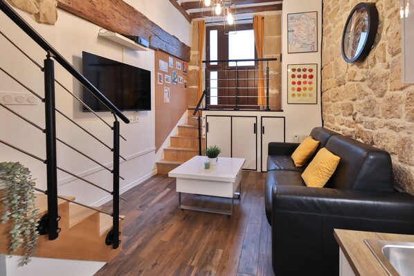 Un salon moderne avec un canapé en cuir noir, une table basse blanche et un escalier doté d’une rampe en bois.
