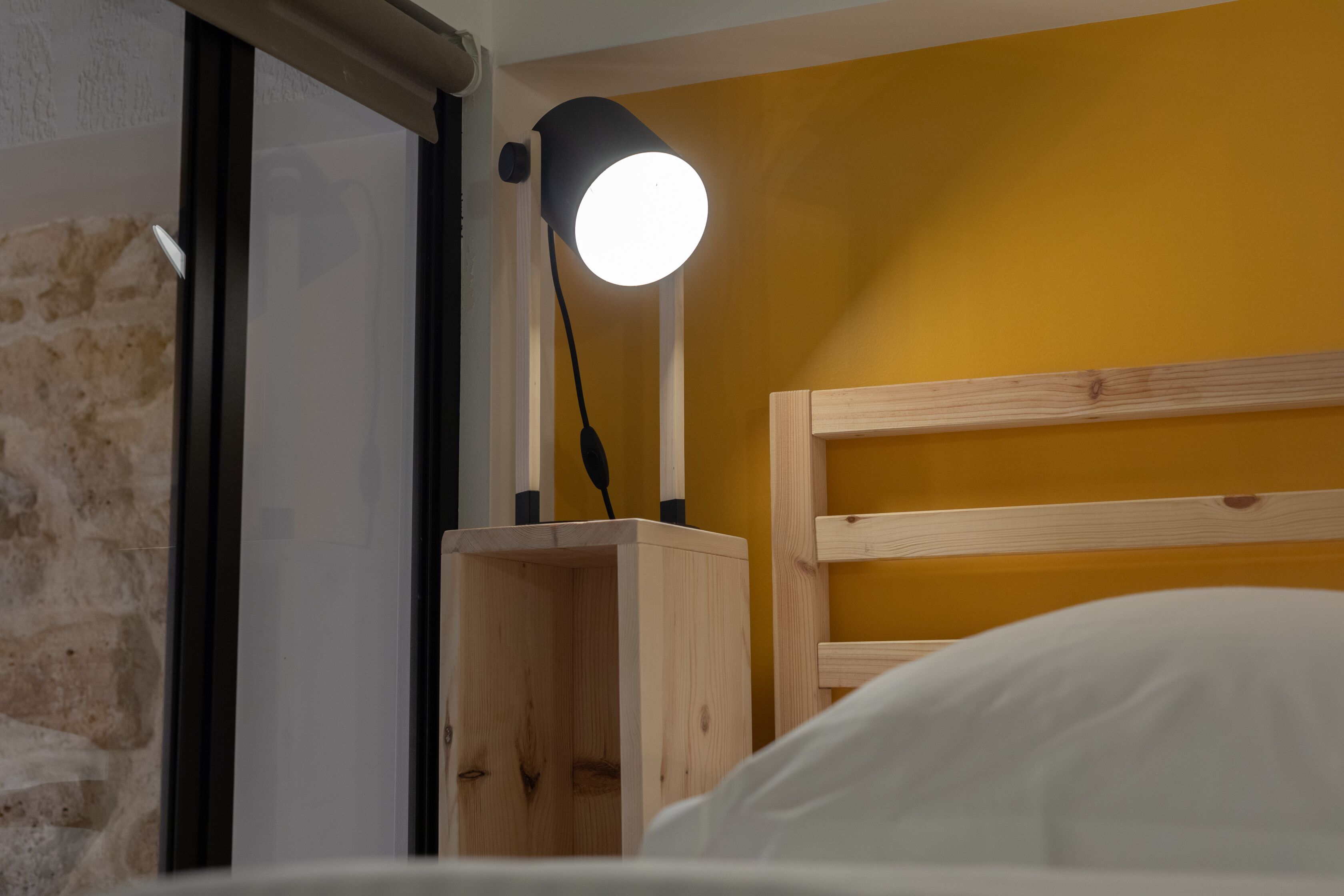 Una cama con cabecera de madera, una mesita de noche con lámpara y una pared de ladrillo.