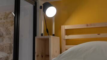 Una cama con cabecera de madera, una mesita de noche con lámpara y una pared de ladrillo.