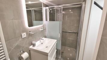 A modern bathroom with a glass-enclosed shower, a white sink, and a mirror.