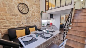 A dining area with a table set for four, a black leather sofa with yellow cushions, and a stone wall.