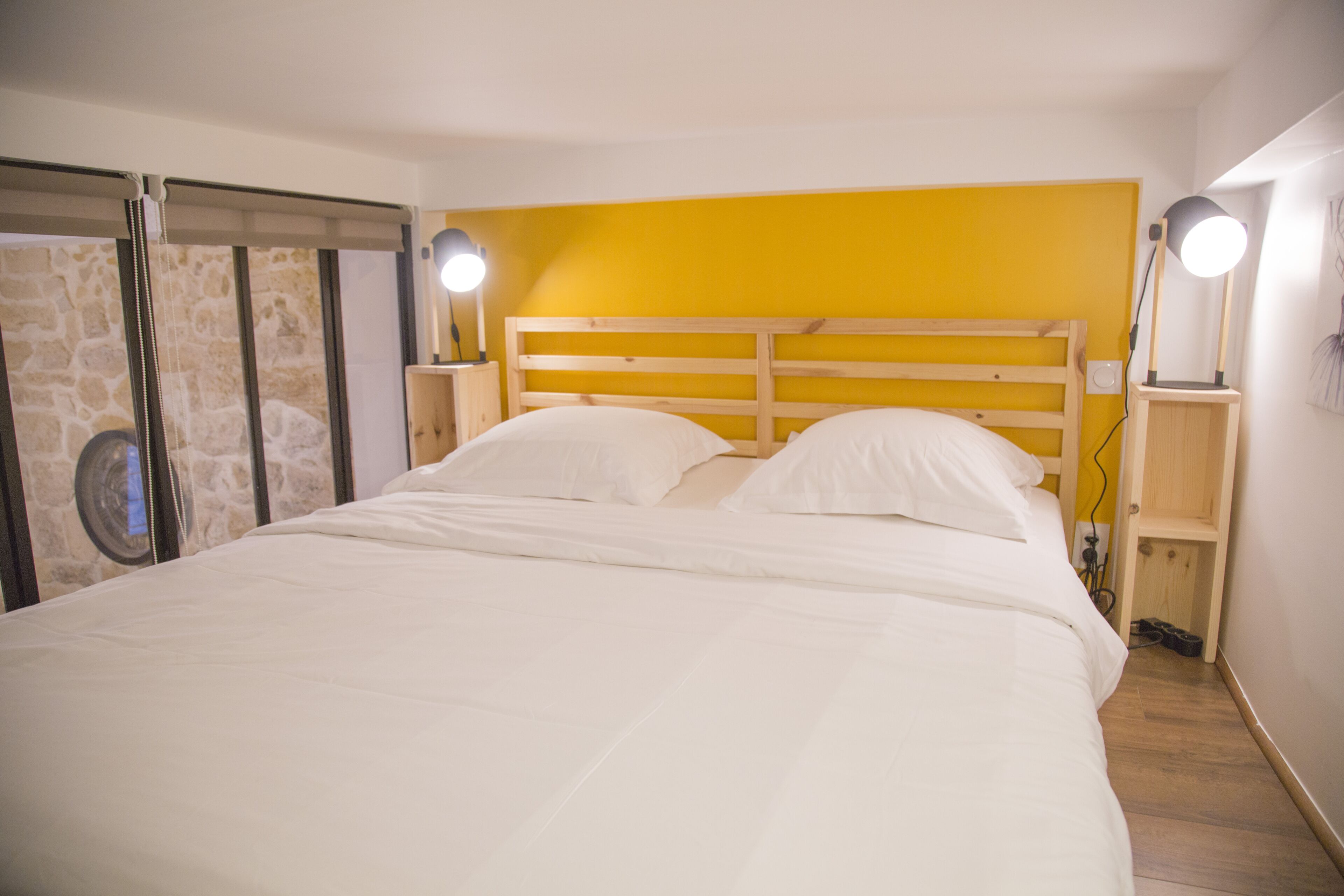 Una cama con sábanas blancas, un cabecero de madera y dos lámparas de noche.