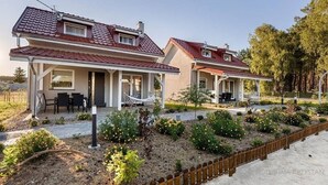 Deux maisons modernes avec des toits recouverts de tuiles rouges, un patio couvert et un jardin aménagé avec diverses plantes et une clôture en bois.