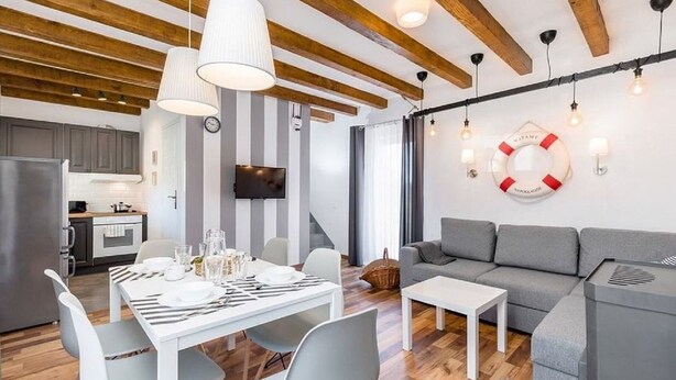 Un salon moderne avec un canapé gris, une table basse blanche et un coin repas avec une table blanche dressée.