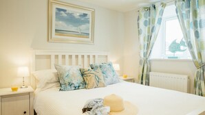 A neatly made bed with floral pillows, a hat, and a blanket on the bed. - 8 Sunday School Court (St Ives)